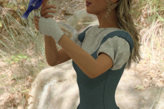 Image title: Wildlife Wonder.  A sunny day in the forest. portrait of a young woman with a blue bird sitting on her finger. She's petting the bird on the chest while the bird sings/talks to her and she listens intently. The woman is wearing a blue dress with a short sleeved blouse under and fingerless summer gloves.She has blond long hair in a half up half down style hair do. Rendered in Daz Studio.